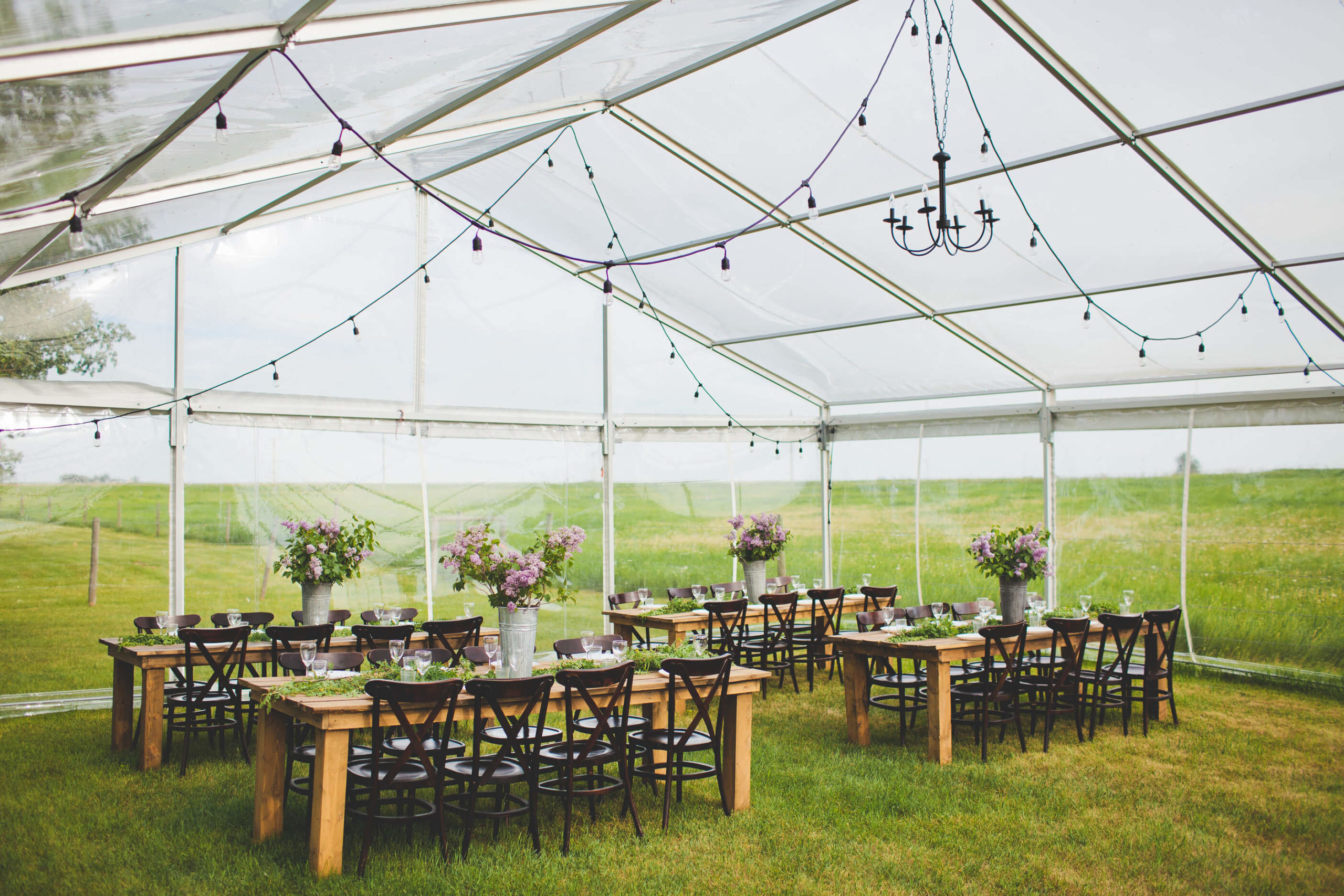 A gathered farm wedding featuring a tent with tables and chairs in the middle of a field.
