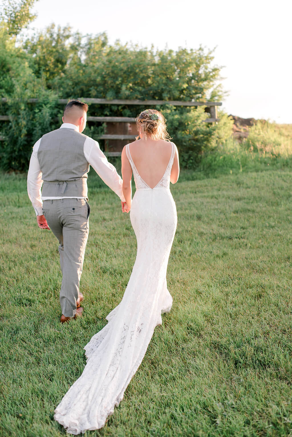 A bride and groom enjoying a farm wedding, walking through a field at sunset.
