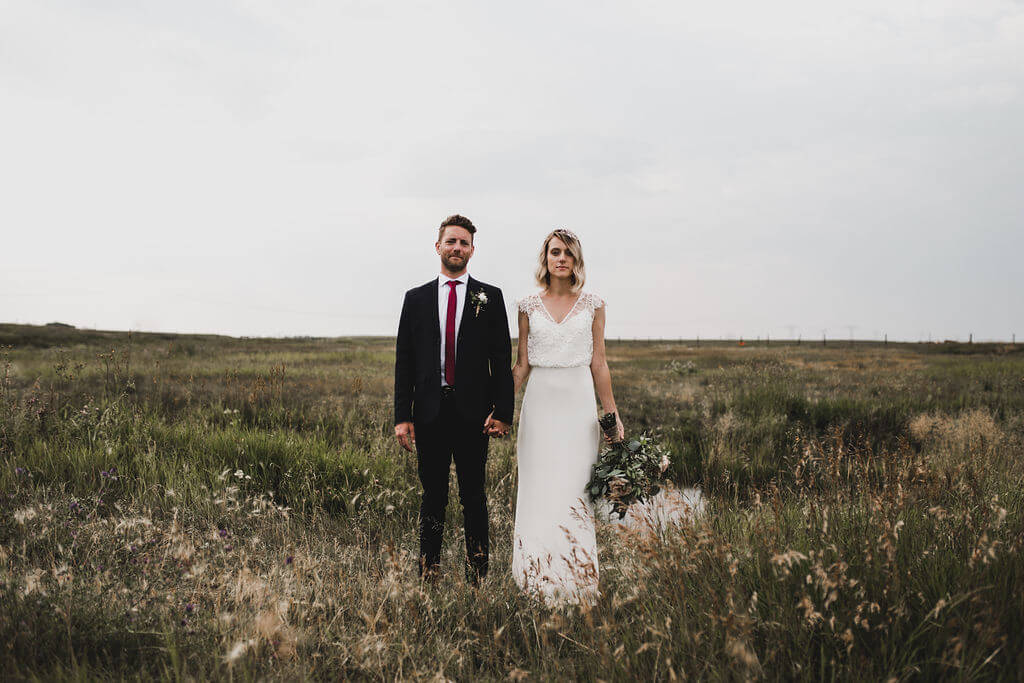 An outdoor bride and groom standing in a field of tall grass at their family wedding.
