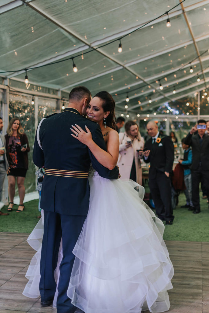 bride and groom first dance while guests watch from the side in a clear tent with globe lighting