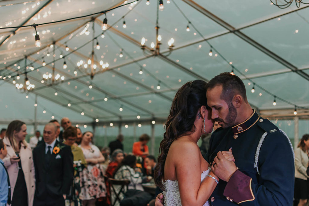bride and grooms first dance surrounded by their guests in a clear tent with hanging chandeliers