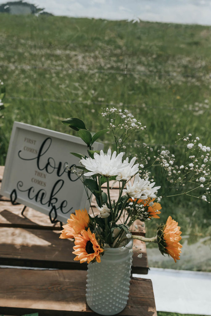 love takes the cake sign with a vase of sunflowers and white flowers beside the sign