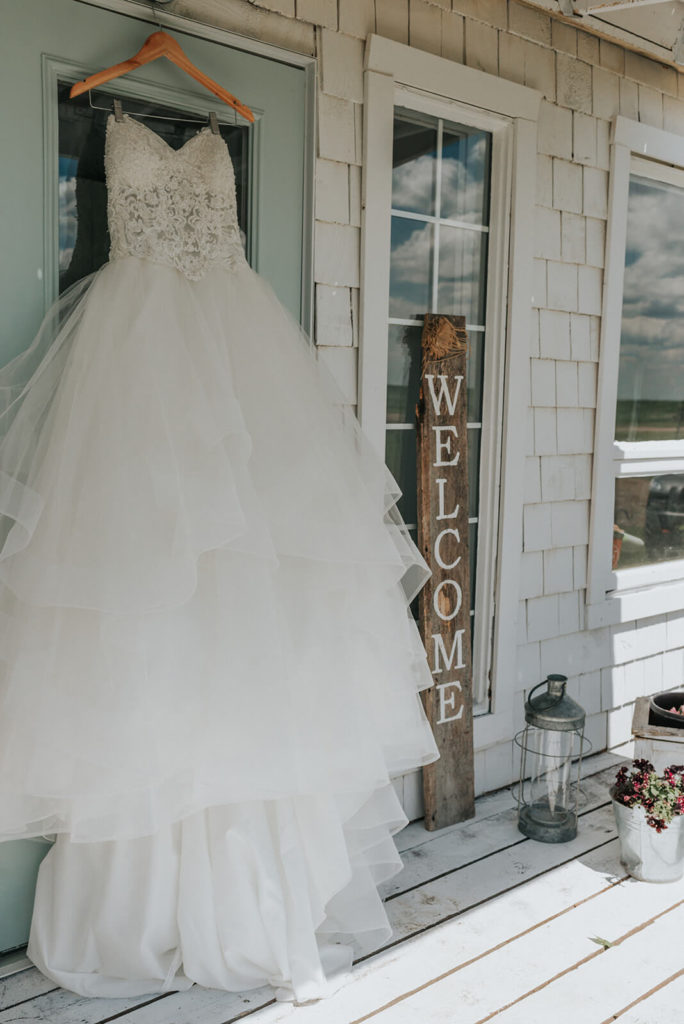 dress hanging on a blue door on the outside of a white cottage with a welcome sign off to the right