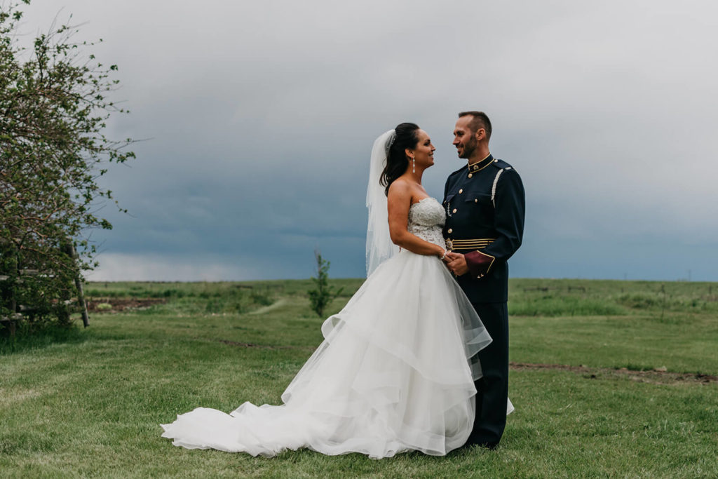 bride and groom standing in a green field with dark grey clouds behind them 