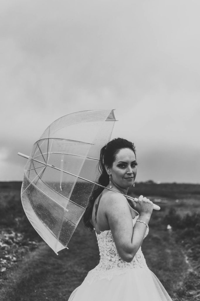 black and white photo of a bride holding a clear umbrella and staring into the camera