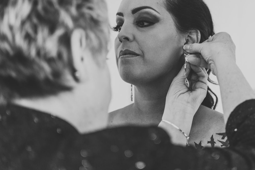closeup of mother putting earrings on the bride