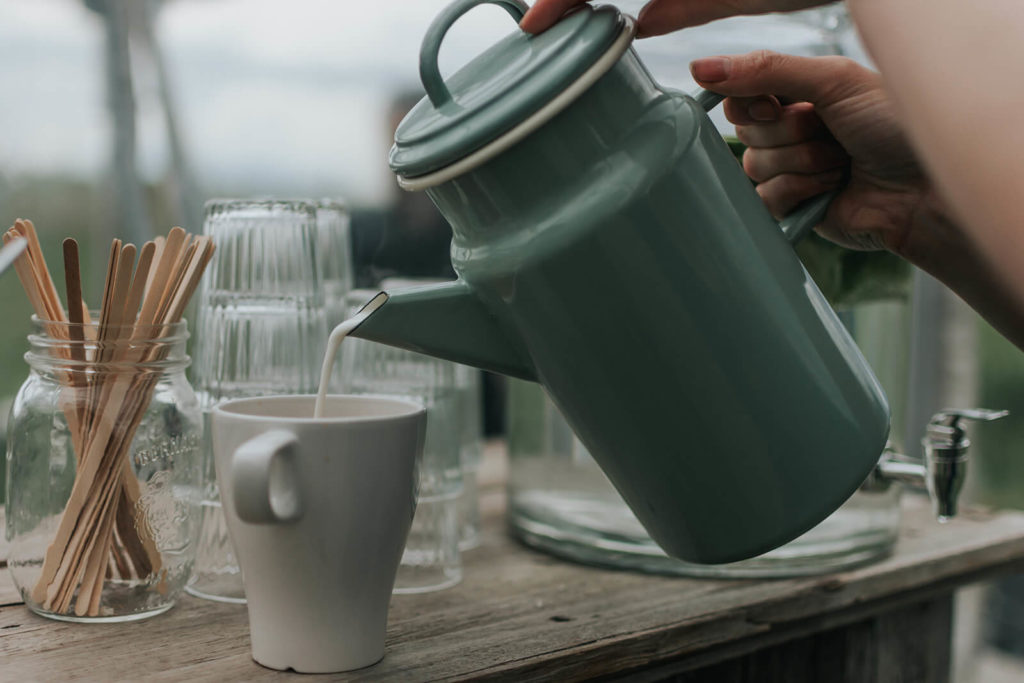 baby blue cream pitcher pouring cream into a white coffee cup, a snack of wood stir sticks sit off to the side