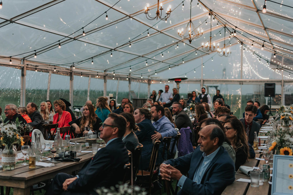 guests seated at long wood harvest tables in the clear reception tent 