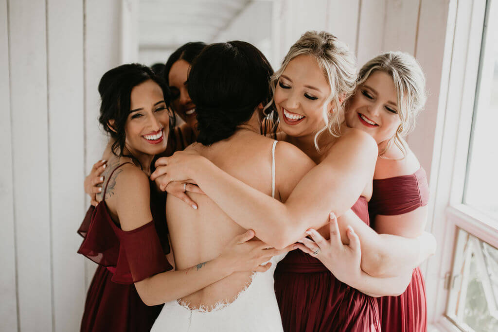 four bridesmaids wearing red dresses giving the bride a group hug