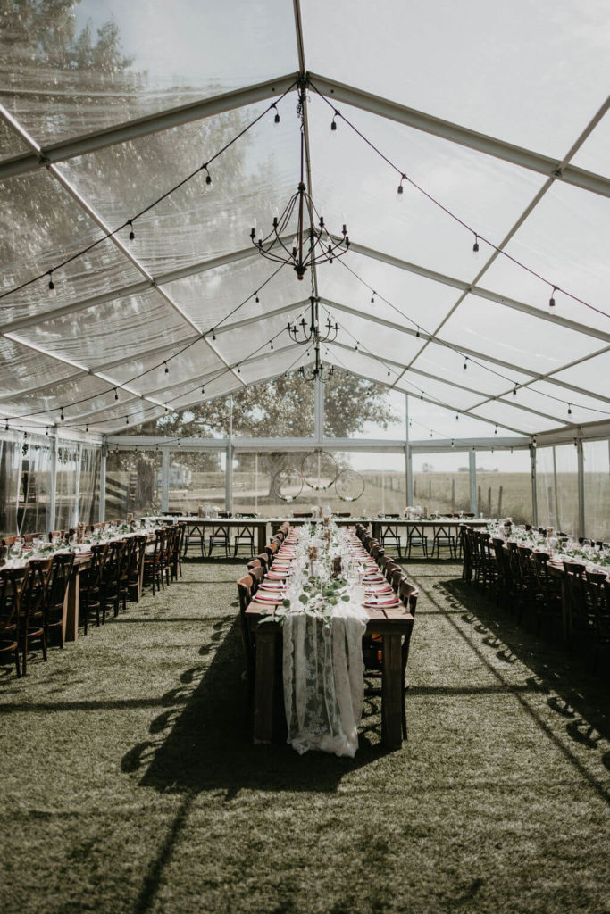 clear tent with wood tables in long rows with lace runners