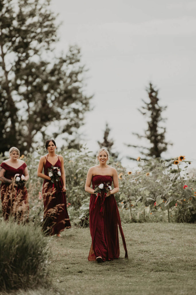 bridesmaids walking down the aisle in their dark red dresses