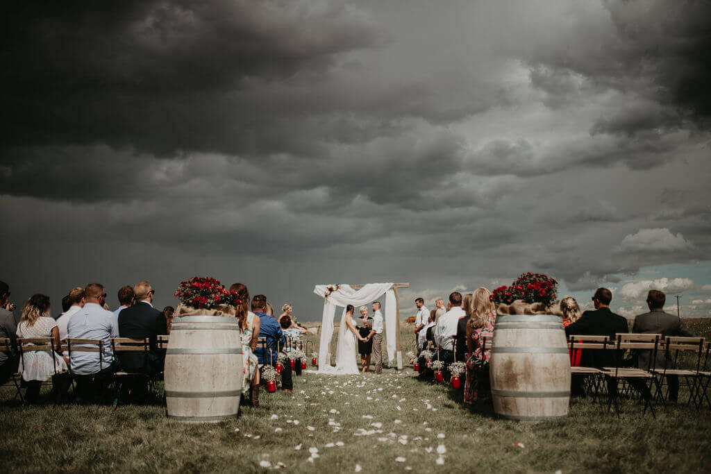 dark storm clouds loom over field ceremony space, large wine barrels sit at the end of the aisle