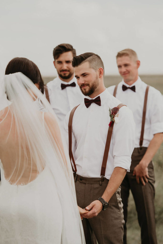 groom at the ceremony looking fondly at his bride, two groomsmen stand behind him