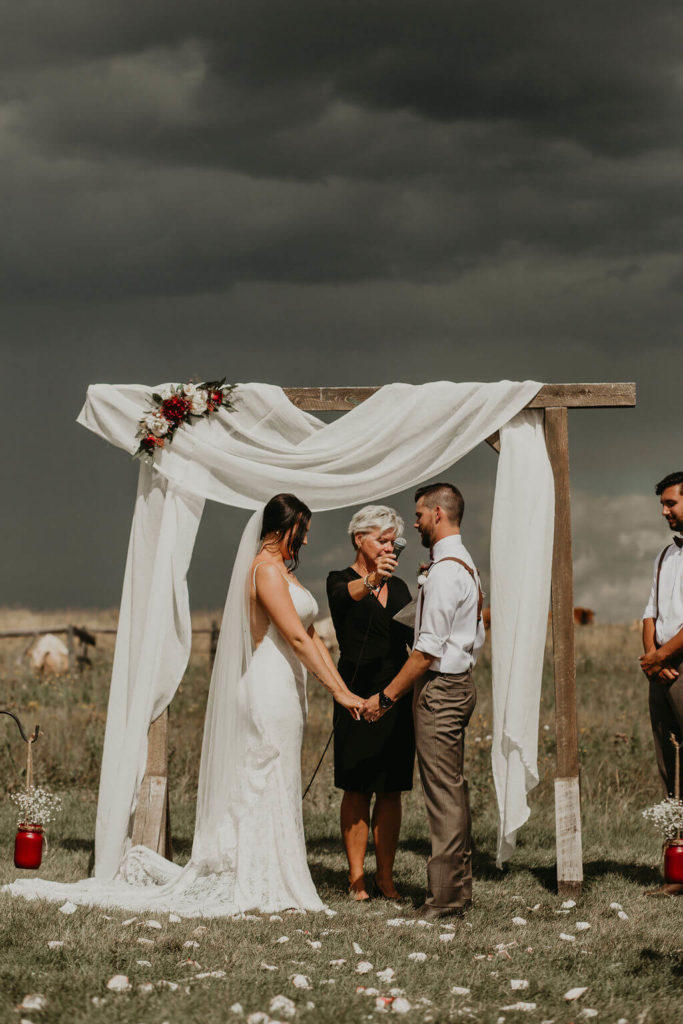 dark skies over ceremony space with a wood arbor decorated in white linen stand over couple