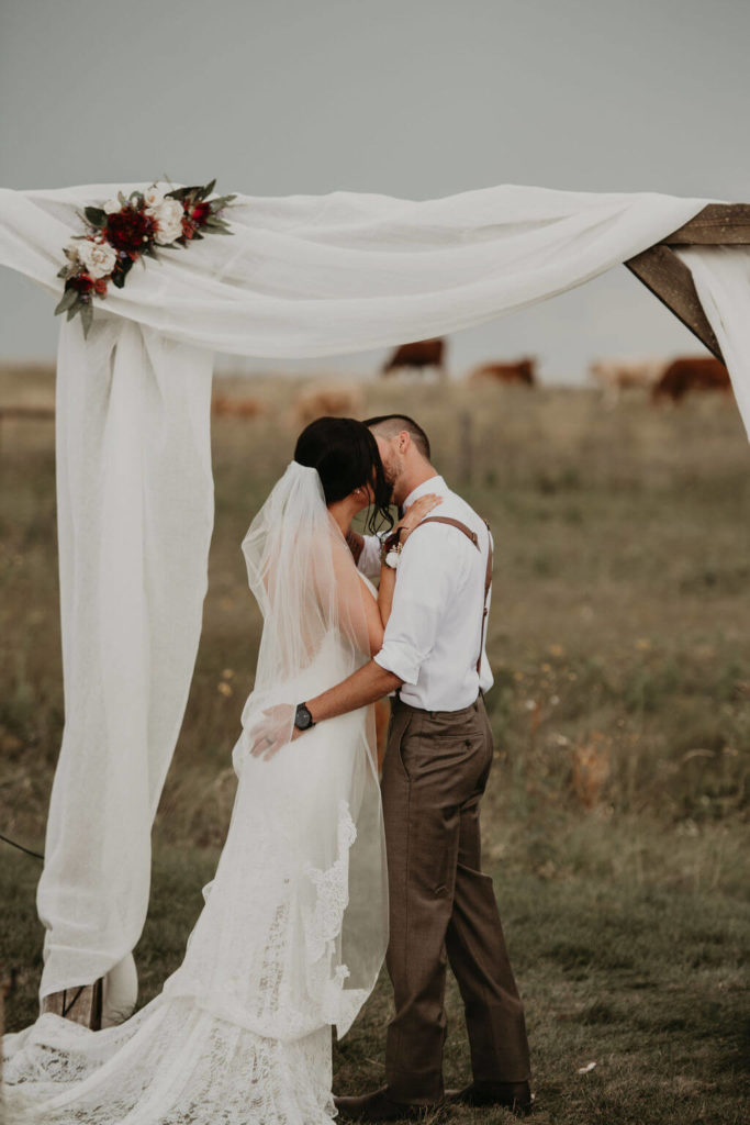 bride and groom kissing under a white linen arbor