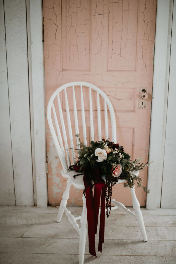 dark moody flower bouquet on a white chair sitting in front of a blush pink door