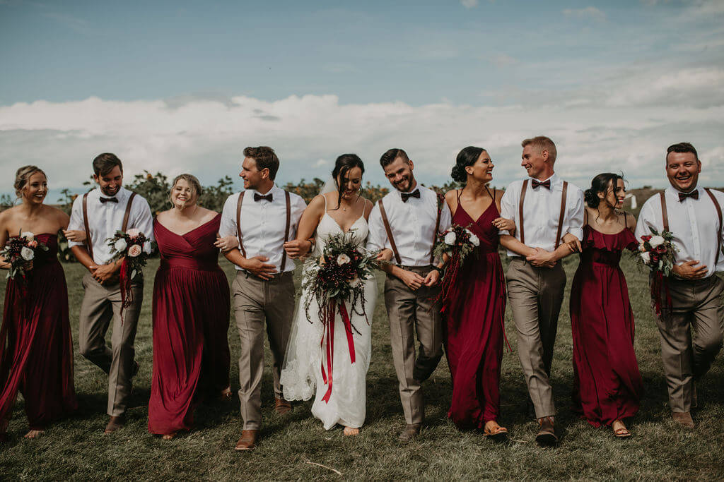 bridal party photos, bride and groom in the middle. girls in red dresses and boys in leather suspenders and gray pants