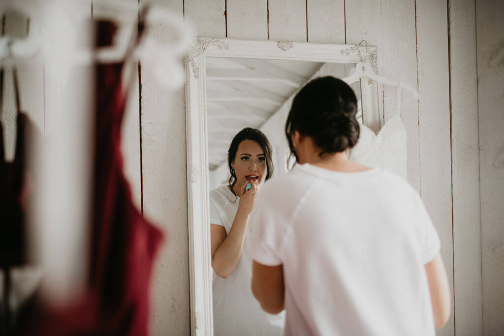 bride putting on her lipstick in a white mirror