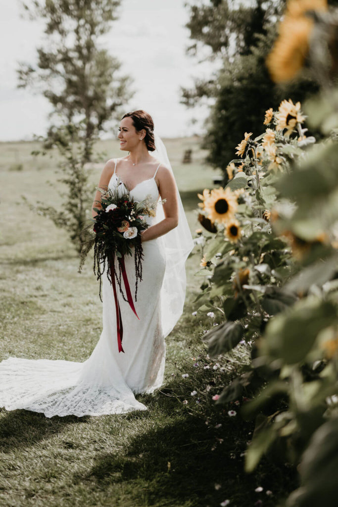 bride holding a dark moody bouquet standing next to a sunflower garden