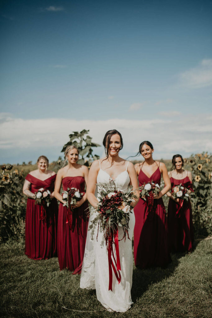 burgundy bridesmaid dresses and bride standing in a sunflower field