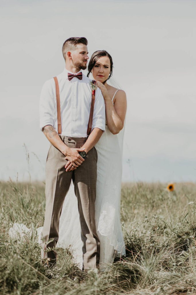 bride standing behind the groom with her hand on his shoulder while they stand in a open prairie field