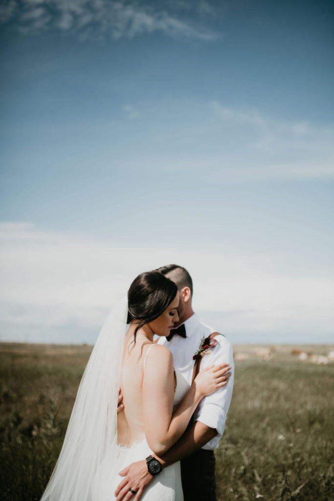 bride and groom standing in a field with big blue sky behind them