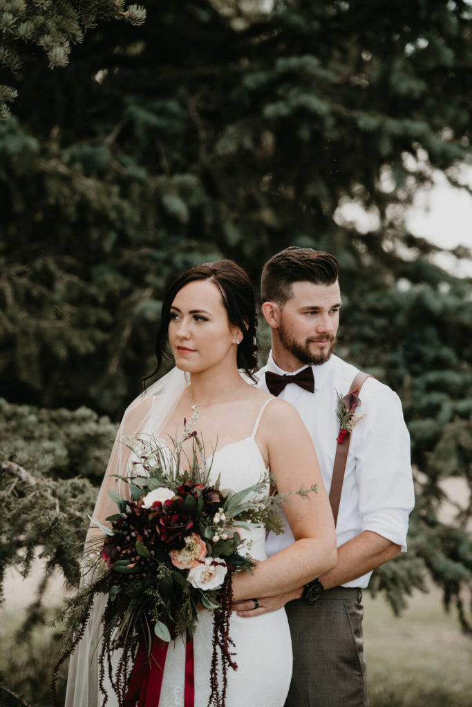 groom standing slightly behind bride while she holds a moody bouquet of flowers
