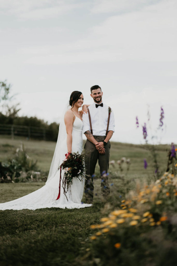 bride and groom standing in a open prairie field, bride has her hand on grooms shoulder