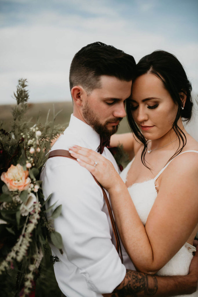 bride and groom closeup standing cheek to cheek in a prairie field