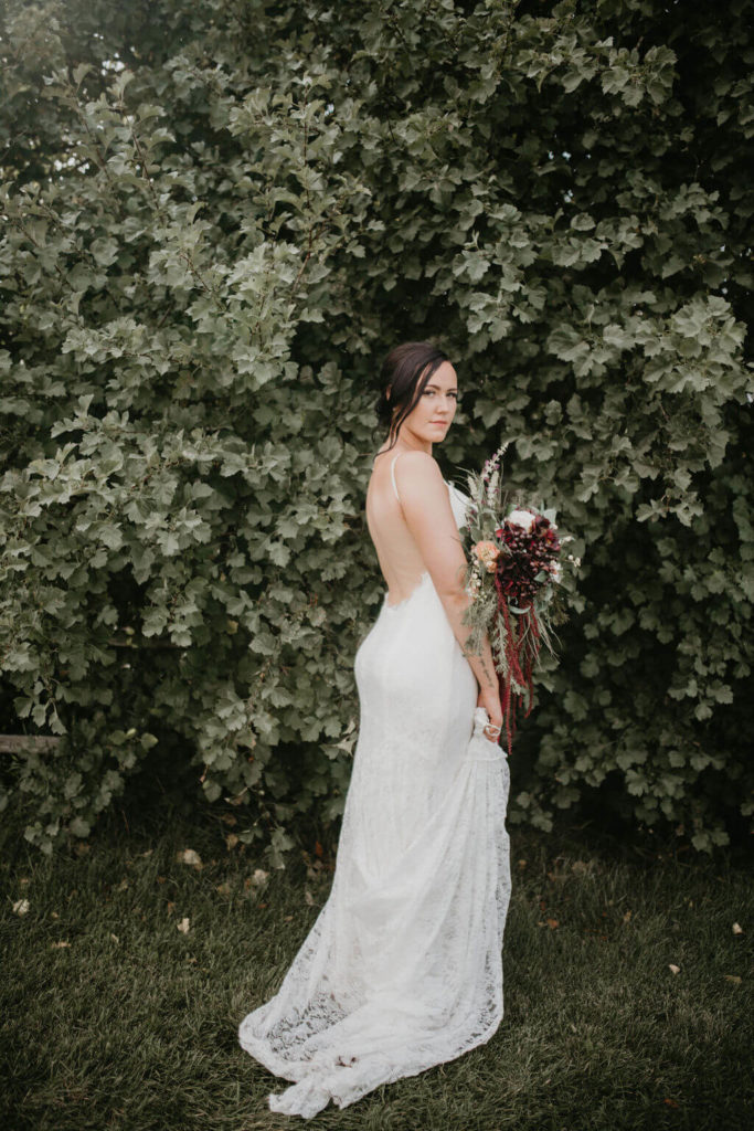bride standing in front of a tree, holding her flowers and showing her low back wedding dress