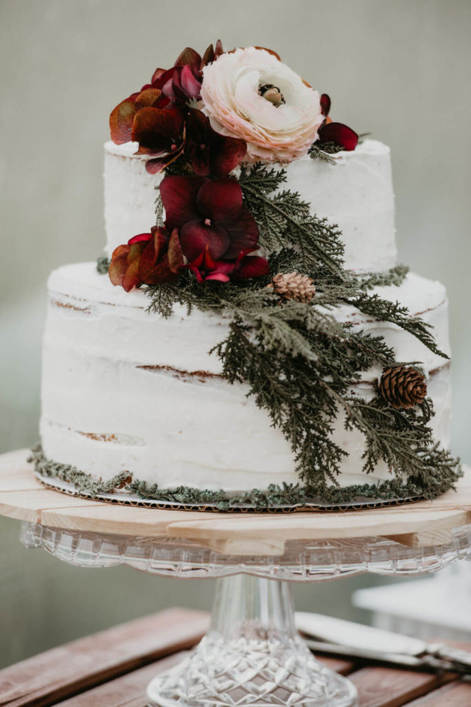 naked wedding cake with greenery and red flowers decorating it
