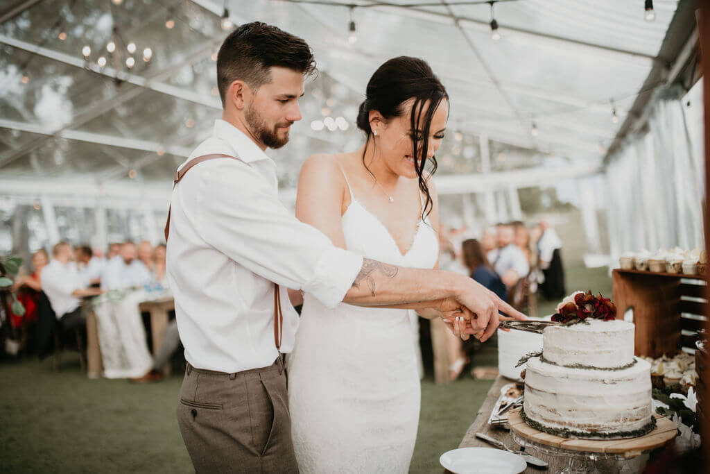 bride and groom cutting their cake in a clear tent