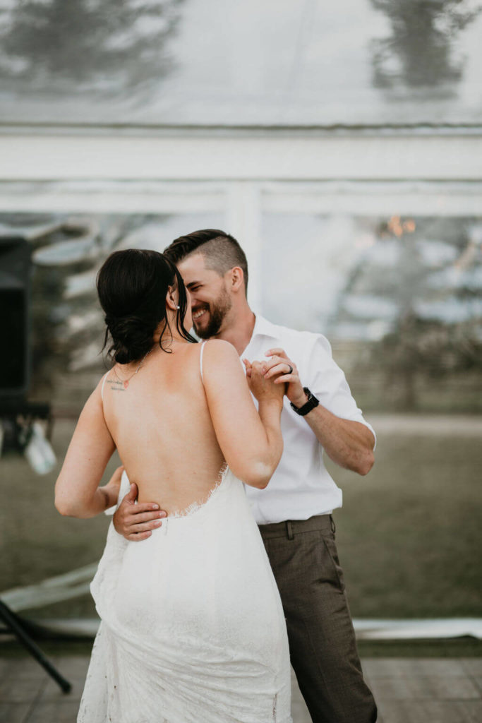 bride and grooms first dance, bride has a low back dress groom in a white shirt and grey pants