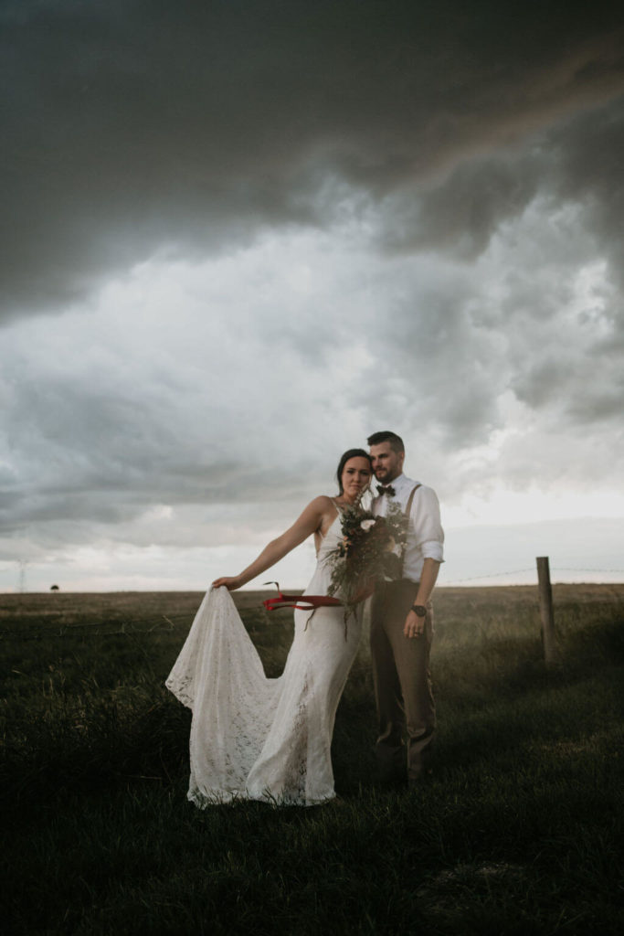 bride and groom standing in a prairie field with dark storm clouds looming
