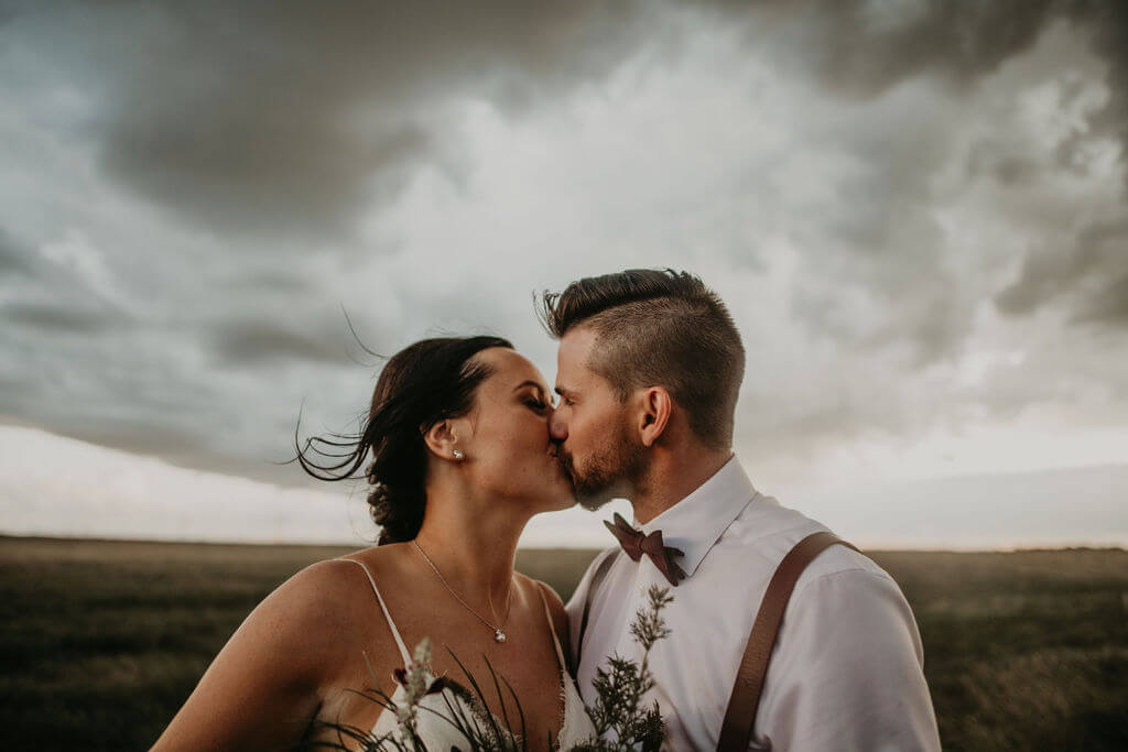 bride and groom kissing in a field with dark clouds