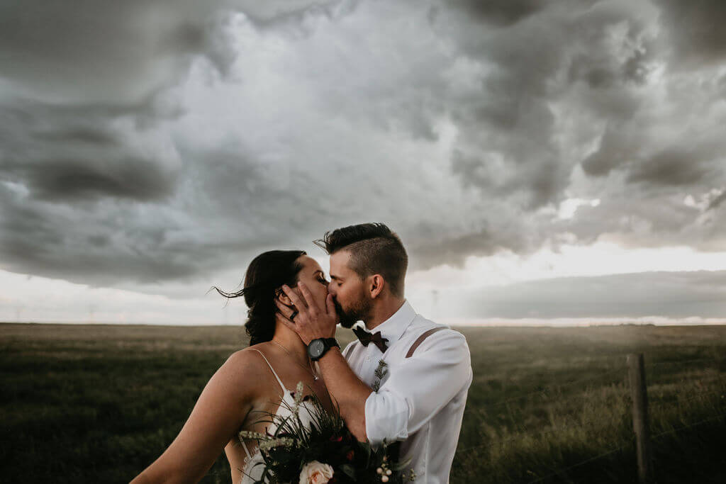 bride and groom kissing in a prairie field and dark clouds looming
