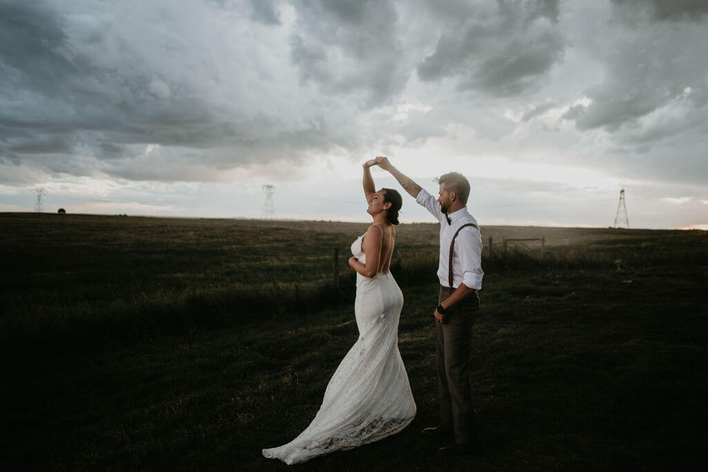 bride and groom twirling in a field with dark cloudy skies