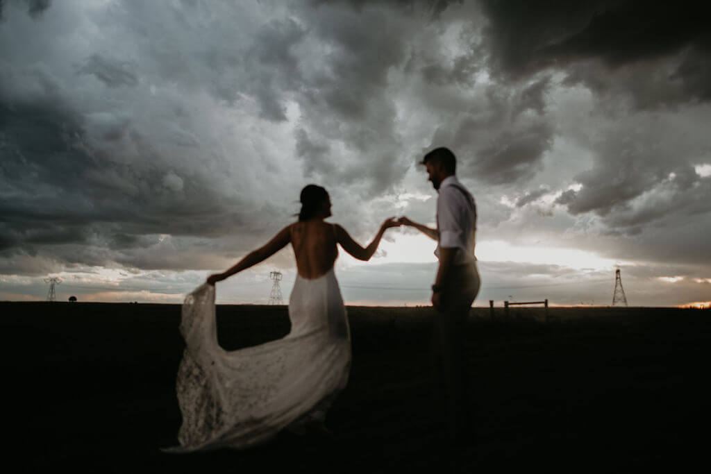 bride and groom dancing in a field with dark clouds and a low sunset