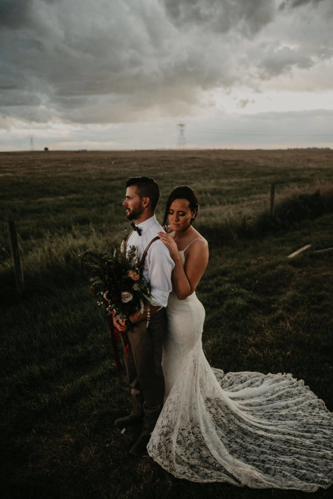 bride and groom standing in a field with storm clouds