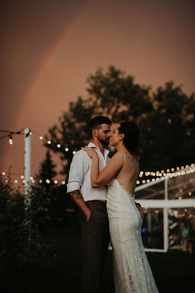 bride and groom posing under a pink sky and rainbow