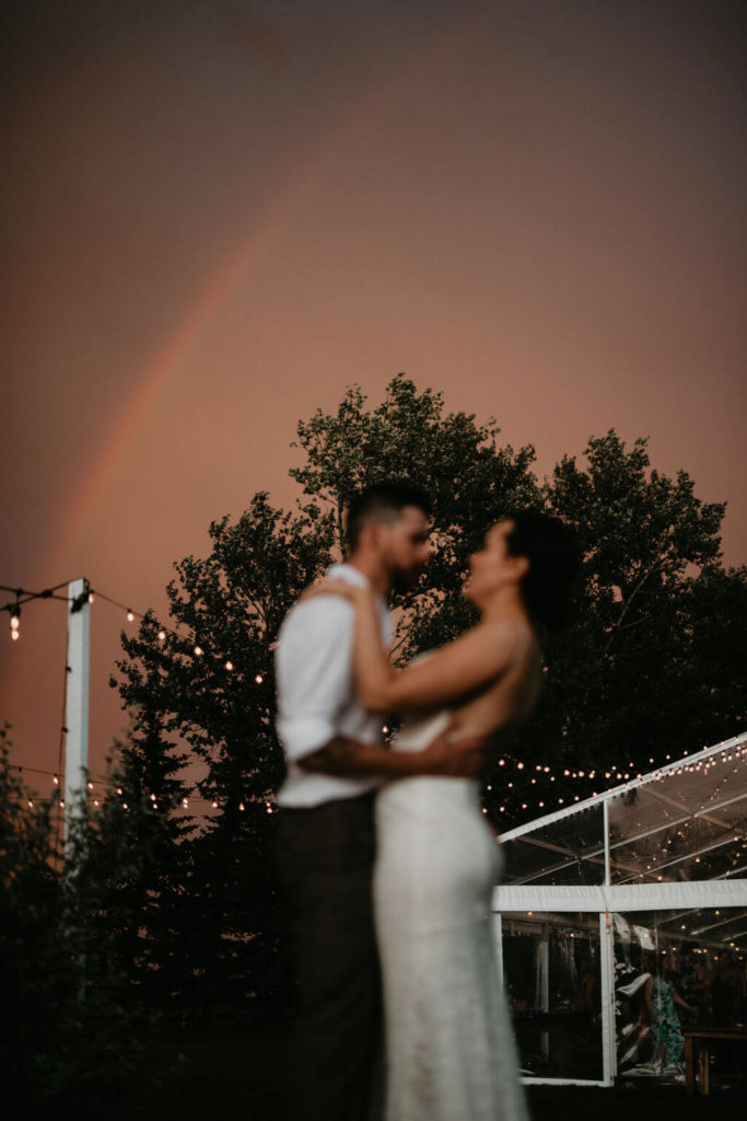 bride and groom standing with a rainbow and pink sky