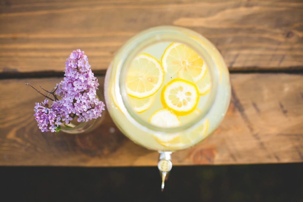 flat lay view of lemonade with real lemon slices and a vase of lilacs 