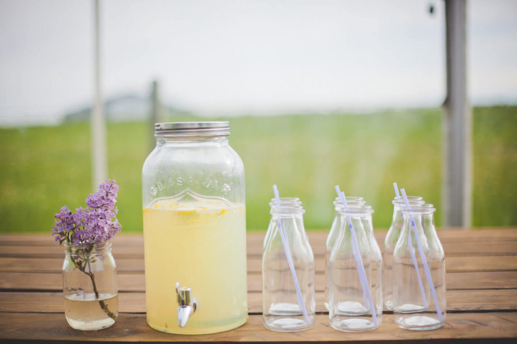 lilacs in a small jar, a pitcher of easy lemonade and multiple juice jars with purple straws.