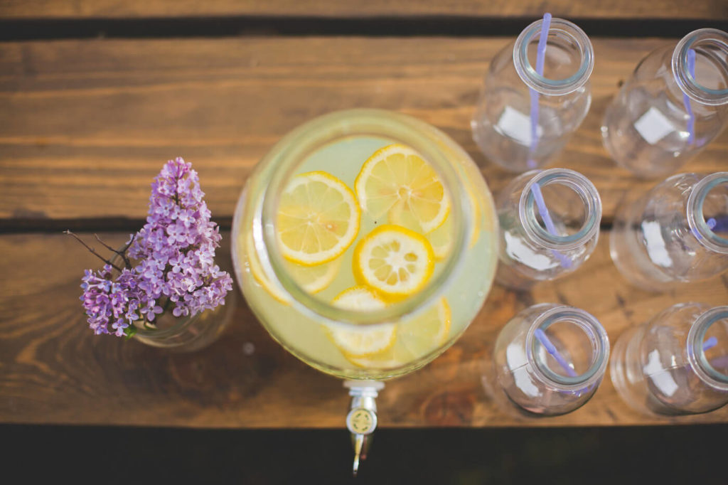 flat lay view of lemonade with real lemon slices, lilacs and milk jars with purple straws