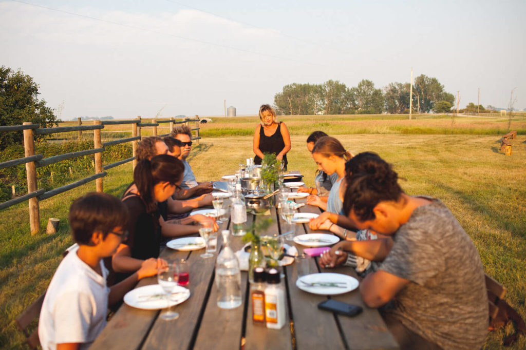 gathering around the dinner table a family sits and says grace in a open field