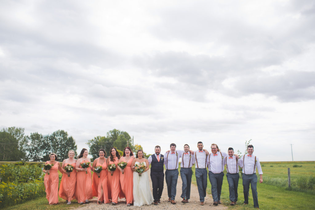 Bridesmaids in vibrant coral-peach flowy dresses with the groomsmen in pink bow ties at this Vibrant wedding at the Gathered.