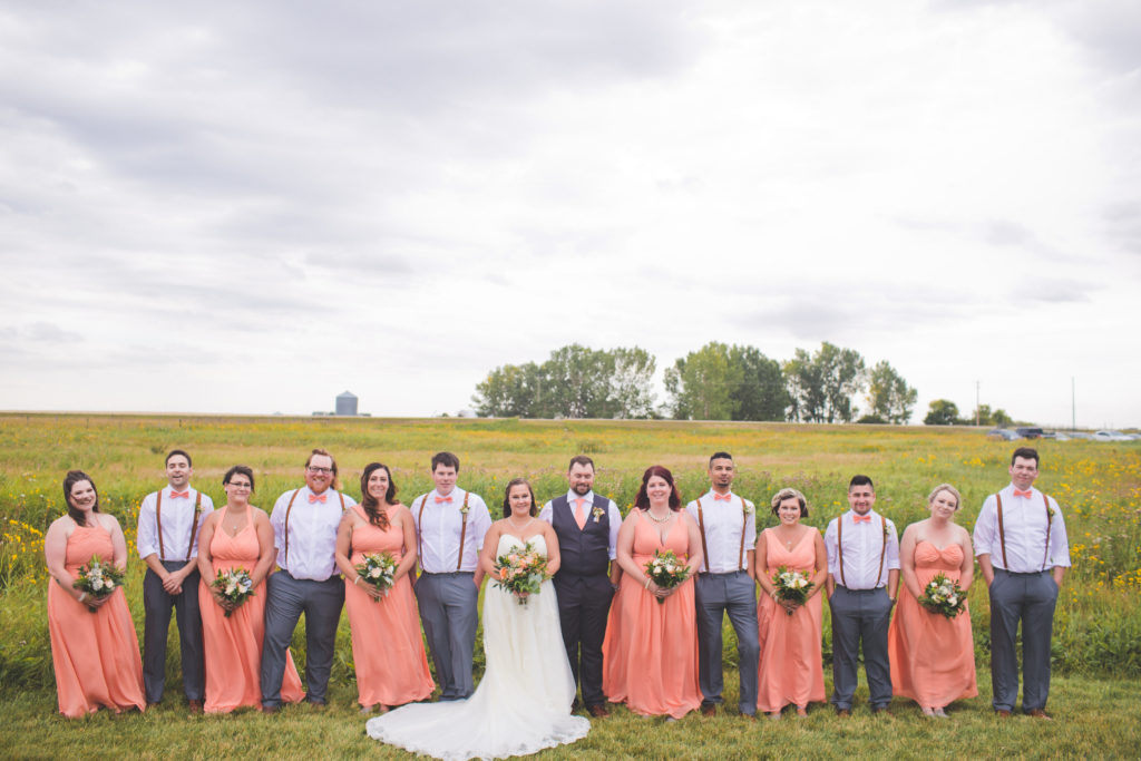 Bridesmaids in vibrant coral-peach flowy dresses with the groomsmen in pink bow ties at this Vibrant wedding at the Gathered.