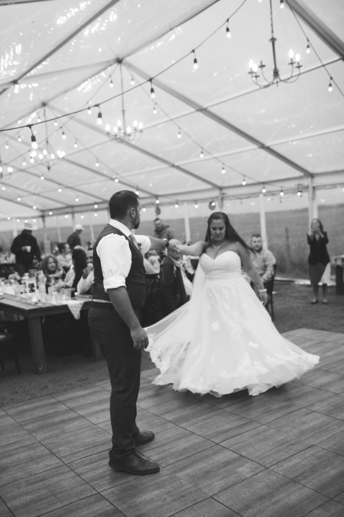 black and white image of a wedding couple twirling on the dance floor for their first dance under clear tent.