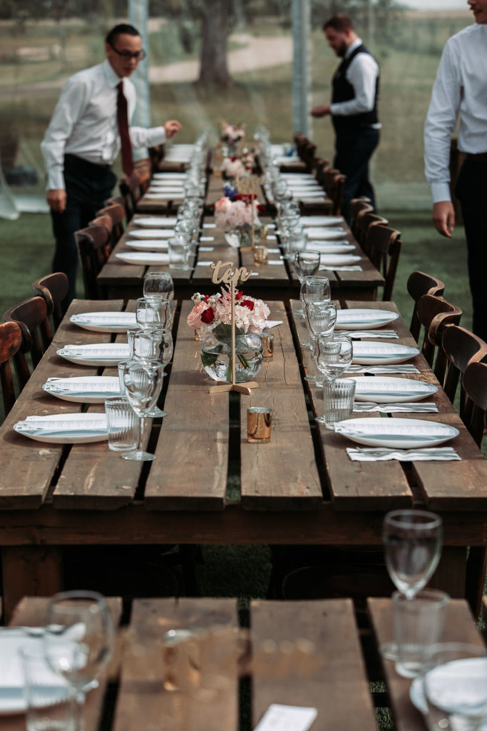 wood harvest tables in a row decorated with white plates, blush pink and burgundy flowers. www.thegathered.ca