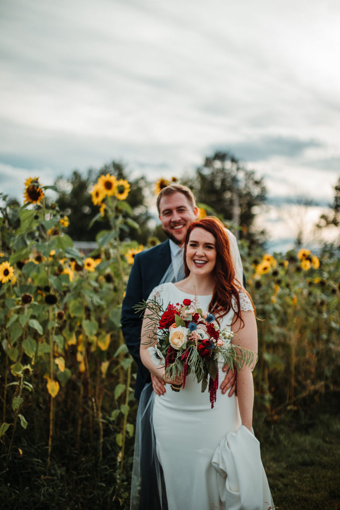 as the sun sets it enhances the jewel toned colors of the brides burgandy bouquet and bright yellow sunflowers at an outdoor wedding in Calgary, Alberta. www.thegathered.ca